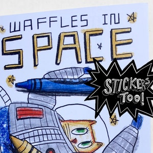 May include: A coloring book cover with a cat astronaut in a rocket ship. The title is "Waffles in Space" in gold letters. The cover also features a blue crayon and a speech bubble that says "Stickers Too!" in black and white.
