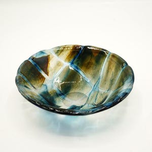 May include: A decorative glass bowl with a unique design. The bowl features a combination of blue, brown, and white colors. The glass has a textured appearance, with a pattern of intersecting lines. The bowl's shape is oval, with a slightly scalloped edge.