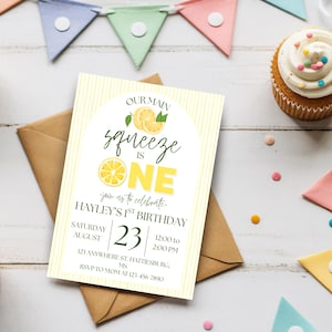 Puede incluir: Una invitación de cumpleaños con temática de limón. La invitación dice "Our Main Squeeze is One" e incluye detalles para el primer cumpleaños de Hayley. La invitación está sobre un fondo blanco con rayas amarillas y junto a un sobre marrón.
