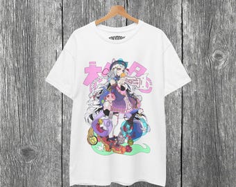May include: White t-shirt featuring a colorful anime-style illustration of a girl with long hair, a hat, and a pink and purple outfit. The design includes Japanese text and various decorative elements.