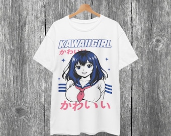 以下が含まれることがあります： 白いTシャツ。青い髪と赤いネクタイをしたアニメの女の子のグラフィックと、青とピンクで「KAWAII GIRL」という文字が描かれています。木製のハンガーに掛けられ、木目調の背景に配置されています。
