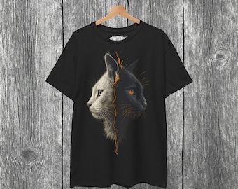 May include: Black t-shirt featuring a split-face cat design. One side is white, the other black, with an orange lightning bolt effect down the middle. The cat's eyes are orange. The shirt is hanging on a wooden hanger.
