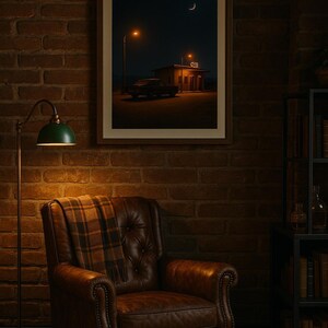 May include: A framed print depicts a nighttime scene with a gas station, car, and crescent moon. A brown leather armchair with a plaid throw sits beneath the print. A green lamp with a brass stand is to the left.