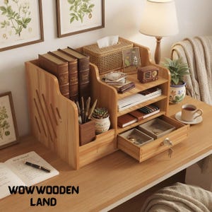 May include: A light wood desk organiser featuring a vertical book storage section, a pen holder, three open shelves, and a pull-out drawer with a key lock. The organiser holds books, a woven tissue box, a small radio, and various office supplies.