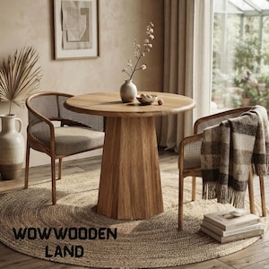 May include: A round wooden dining table with a faceted pedestal base, accompanied by two chairs featuring cane backrests and beige cushions. A ceramic vase with branches sits on the table, while a plaid throw blanket rests on one chair.