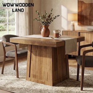 May include: A square wooden dining table with a thick pedestal base, accompanied by two chairs with dark grey upholstered seats. A beige table runner, a terracotta vase with dried foliage, and two stacked mugs sit on the table. Text reads WOWWOODEN LAND.