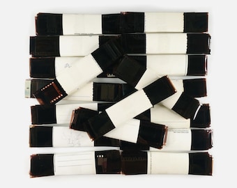 May include: A collection of vintage 35mm film strips, each encased in a white paper sleeve. The film strips are black and brown, and the sleeves have handwritten notes. The arrangement is a mix of horizontal and vertical stacks.