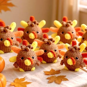 Puede incluir: Una colección de pequeñas figuras de pavo redondas tejidas a ganchillo con hilo marrón. Cada pavo presenta plumas de cola amarillas y naranjas, un pico amarillo y una carúncula roja. Las figuras tienen ojos de plástico negro y están agrupadas.
