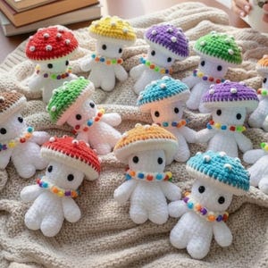 May include: A collection of small, handmade crochet mushroom figures with white bodies and colorful caps. Each figure features a white stem, a rounded cap in various colors like red, yellow, purple, green, and blue, and a necklace of small beads.