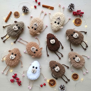 May include: A collection of ten crocheted sheep ornaments in various shades of brown, beige, and white. Each sheep features a textured body, a small cream-colored face with black eyes, and thin limbs tipped with small pink beads for decorative accents.