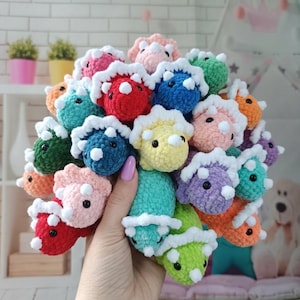 Puede incluir: Una colección de coloridos dinosaurios triceratops de ganchillo en varios tonos, incluyendo rojo, azul, verde y rosa. Cada dinosaurio tiene un volante blanco y pequeños ojos negros. Los dinosaurios se sostienen juntos en un grupo.