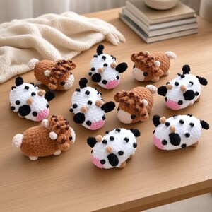 May include: A collection of nine small, crocheted plush animals shaped like cows and highland cattle. The figures feature soft yarn textures, black bead eyes, and distinct color patterns including solid brown, white with black spots, and white with brown spots.