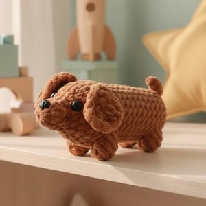 May include: A small, brown, crocheted plush dog toy with a textured, yarn-based surface. The figure features two round black plastic eyes, a small black plastic nose, floppy ears, and a short, curled tail, crafted in a soft, stuffed style.