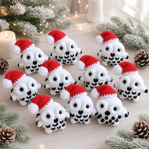 May include: A collection of ten small, white crocheted owl figurines, each wearing a miniature red and white Santa hat. The owls feature black embroidered details on their bodies and large black eyes, arranged on a light surface.