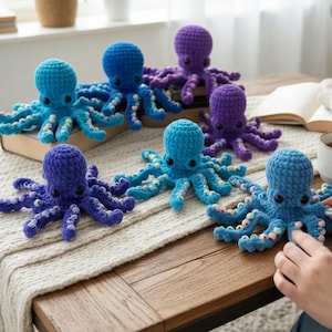 May include: A collection of handmade crochet octopuses in various shades of blue and purple. Each octopus features a rounded head, eight tentacles, and small black eyes. The tentacles are adorned with colorful accents. They are arranged on a wooden table.