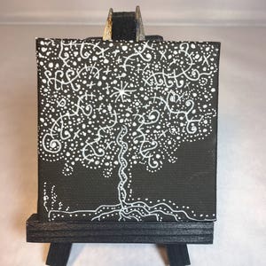 May include: A small black canvas painting with a white tree design. The tree is made up of white dots, lines, and swirls. The painting is on a small easel.