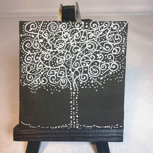 May include: A small black canvas painting of a white tree with a swirling design on a black easel.