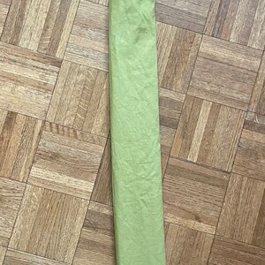 May include: A long, green fabric bag tied with a blue ribbon. The bag is lying flat on a wooden floor.