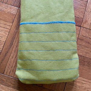 May include: A green fabric towel with blue stripes. The towel is folded in half and has a blue trim around the edges.