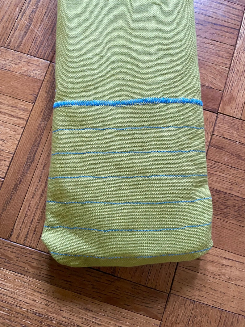 May include: A green fabric towel with blue stripes. The towel is folded in half and has a blue trim around the edges.