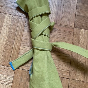 May include: A green canvas bag rolled up and tied with a green strap. The strap is tied in a knot and the ends are frayed.