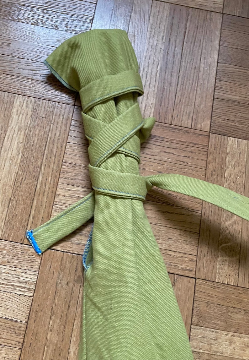May include: A green canvas bag rolled up and tied with a green strap. The strap is tied in a knot and the ends are frayed.