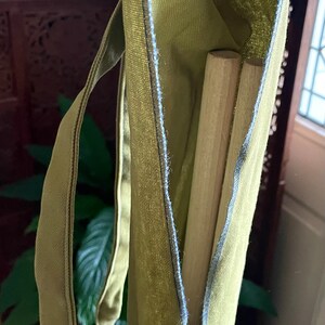 May include: A green canvas bag with a blue seam and a label that says "All Earthlings" with an arrow pointing to the right. Two wooden dowels are inside the bag.