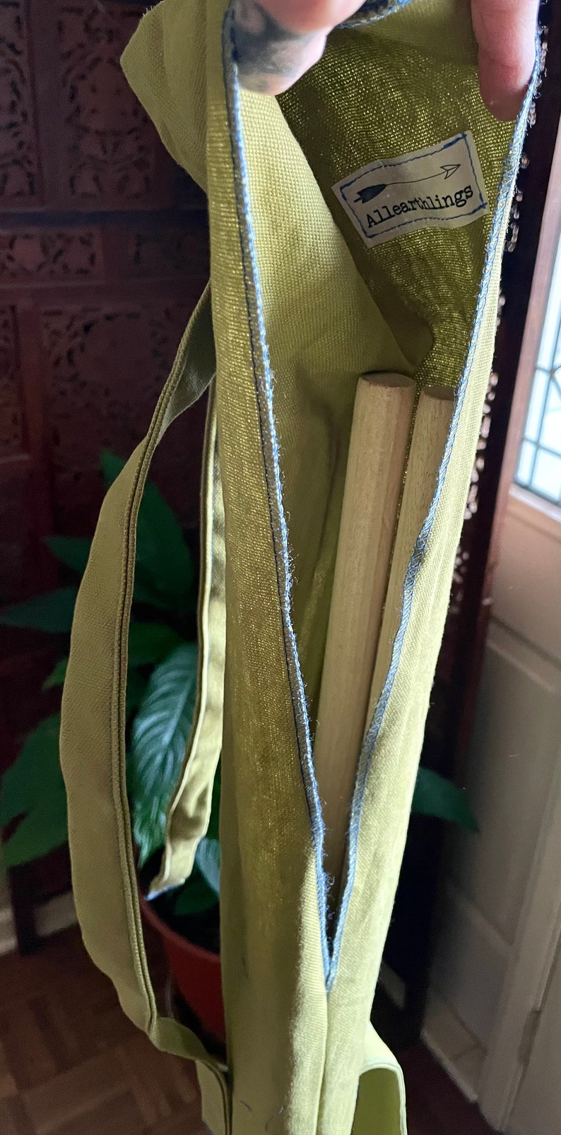 May include: A green canvas bag with a blue seam and a label that says "All Earthlings" with an arrow pointing to the right. Two wooden dowels are inside the bag.