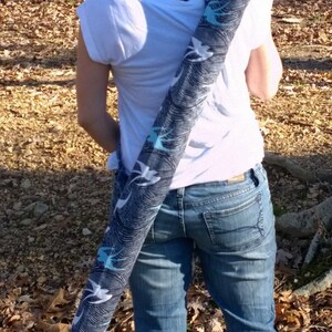May include: A woman wearing a white t-shirt and blue jeans is carrying a black and white patterned bag over her shoulder.