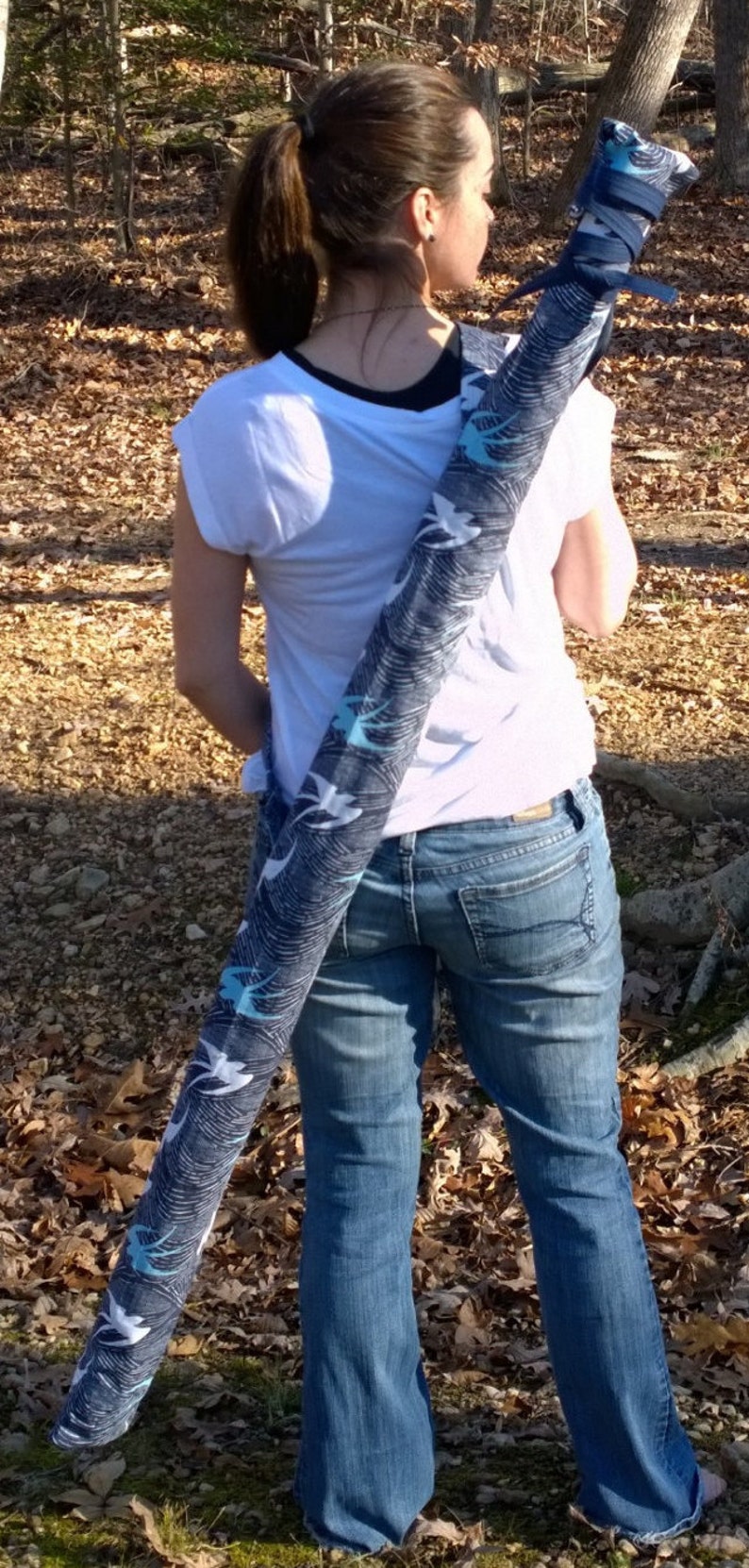 May include: A woman wearing a white t-shirt and blue jeans is carrying a black and white patterned bag over her shoulder.