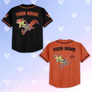 Op de afbeelding: Twee honkbalshirts, &eacute;&eacute;n zwart en &eacute;&eacute;n oranje, met een cartoon vos karakter. De shirts hebben de tekst "YOUR NAME" op de rug en een vos afbeelding. De mouwen hebben oranje en zwarte randen.