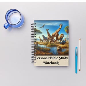 Peut inclure: Cahier à spirales avec une couverture illustrant la faune africaine, notamment des girafes, des zèbres et des lions. Le cahier porte l'inscription "Personal Bible Study Notebook". Un stylo bleu, un stylo blanc et un verre bleu sont également visibles.