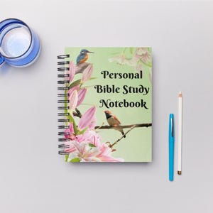 May include: A spiral-bound notebook with the text "Personal Bible Study Notebook" on the cover. The cover features a floral design with birds. A blue mug, a blue pen, and a white pencil are also in the image.