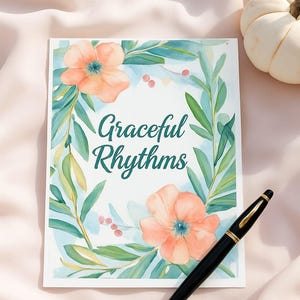 Op de afbeelding: Een wenskaart met de tekst "Graceful Rhythms" omringd door aquarelbloemen en bladeren. Een zwarte pen met gouden accenten ligt op de kaart. Op de achtergrond een kleine witte pompoen.