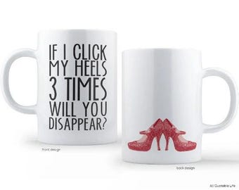 Può includere: Due tazze in ceramica bianca. Una tazza ha il testo "IF I CLICK MY HEELS 3 TIMES WILL YOU DISAPPEAR?" in nero. L'altra tazza ha un design di scarpe con tacco alto rosse. Un'idea regalo divertente.