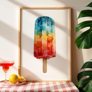 May include: A framed art print of a colorful popsicle with a wooden stick. The popsicle features a gradient of colors, including red, orange, yellow, blue, and green. A red cocktail with a lime garnish and a plate with lemons are on a table.