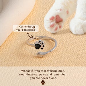 May include: A silver ring with a black paw print design. The ring is adjustable and features the word "Mellow" and "5925" engraved on it. The text "Customize your pet's name" is also present.