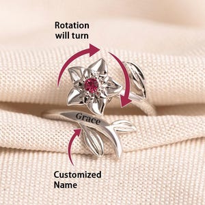 Könnte beinhalten: Ein silberfarbener Ring mit einem Blumendesign und einem roten Edelstein in der Mitte. Der Ring hat ein Blumen- und Blattdesign mit dem eingravierten Namen "Grace". Der Text "Customized Name" ist ebenfalls sichtbar.