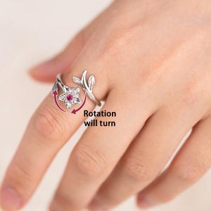 May include: A silver-colored ring with a floral design, featuring a rotating star-shaped centerpiece with a red gemstone. The ring has a leaf and branch design. The text "Rotation will turn" is also visible.