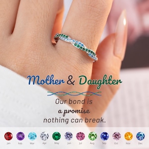 May include: A silver ring with a wave design, adorned with green, blue, and clear gemstones. The ring is on a finger, with text that reads "Mother & Daughter" and "Our bond is a promise nothing can break."