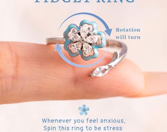 May include: A silver fidget ring featuring a rotating flower design. The flower has a light blue enamel outline and clear crystal petals. The ring's text says "FIDGET RING" and "Rotation will turn". The ring is designed to help with anxiety.
