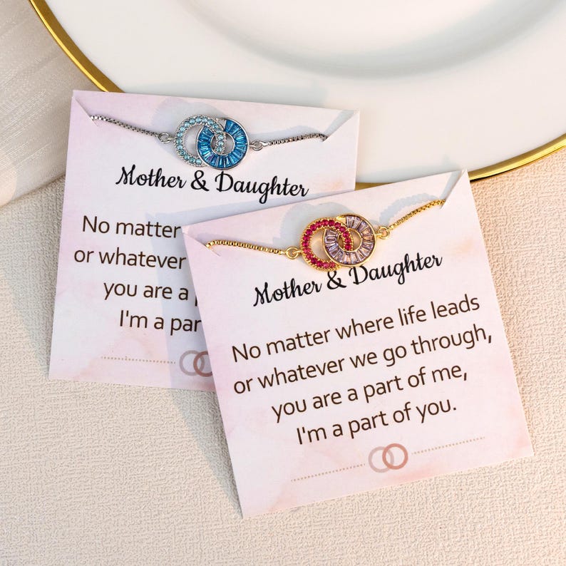 May include: Two bracelets with interlocking circles, one silver with blue gems, the other gold with red and purple gems. Each bracelet is on a card that reads "Mother & Daughter" and a sentimental message.