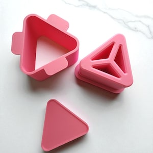 Puede incluir: Tres cortadores rosas de plástico para moldear arroz onigiri. Uno es de forma triangular con un asa, otro es un triángulo con soportes interiores y el tercero es un triángulo macizo. Los cortadores están diseñados para hacer bolas de arroz triangulares.