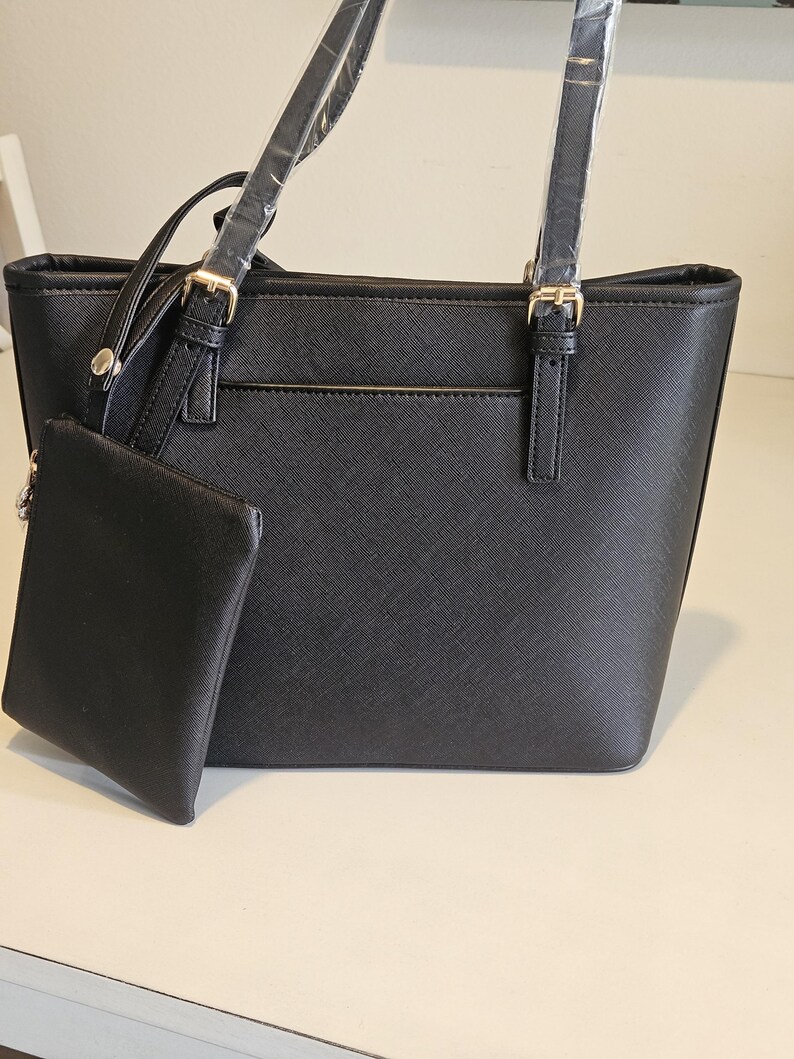 May include: Black tote bag with a matching small pouch. The bag has two top handles and a detachable shoulder strap. Gold-colored hardware accents the bag's design. The bag is made of a textured material.