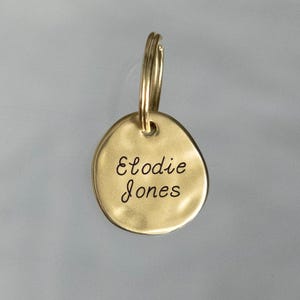 May include: Gold-colored metal keychain with a round tag engraved with the name "Elodie Jones".