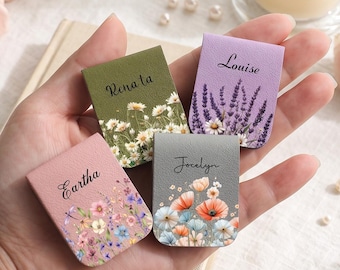 May include: Four rectangular magnetic bookmarks featuring floral designs and personalised names. The olive green bookmark reads Renata, the lavender one reads Louise, the pink one reads Eartha, and the grey one reads Jocelyn, each with unique flower prints.