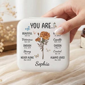 Puede incluir: Caja de joyería cuadrada blanca con las palabras "YOU ARE..." y texto inspirador. Presenta un diseño floral y detalles de mariposas. El nombre "Sophia" está impreso en la parte inferior.