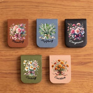 Può includere: Una collezione di segnalibri in pelle personalizzati, ognuno con un design floreale e un nome. I segnalibri sono in vari colori, tra cui marrone, blu e verde. I nomi "Brinley", "Jeffrey", "Dayana", "Carey" e "Carter" sono visualizzati.