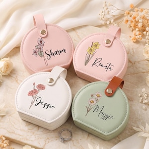 May include: Four round jewelry cases with snap closures, featuring pastel colors of pink, white, and sage green. Each case is personalized with a floral illustration and a name: Sharon, Renata, Jessie, or Maggie, printed in black script.
