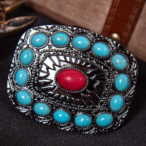 May include: Silver-toned rectangular belt buckle with turquoise and red stone accents. The buckle features an oval red stone in the center, surrounded by turquoise stones. The design has an ornate, vintage aesthetic.